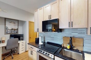 A kitchen with wooden cabinets, a microwave, a stove, and a small dining area with a chair and table. - Stunning ski studio with pool, hot tub, firepit & mountain views - walk to lifts (Steamboat Springs)