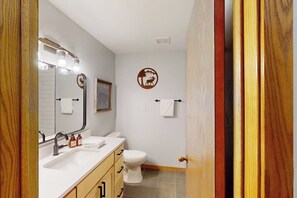 A bathroom with a white sink, mirror, and toilet. There is a towel rack on the wall and a framed picture above the toilet. - Stunning ski studio with pool, hot tub, firepit & mountain views - walk to lifts (Steamboat Springs)