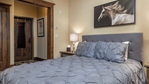 Ein Schlafzimmer mit einem großen Bett, einem Kopfteil, einem Nachttisch, einer Lampe, einem Bilderrahmen mit dem Motiv eines Pferdes und einer Holztür.