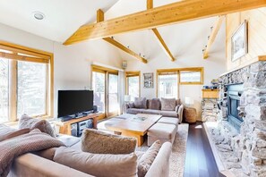 Ein geräumiges Wohnzimmer mit Kamin aus Stein, Holzbalken und großen Fenstern.
