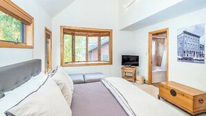 Una camera da letto con un letto, una televisione, una cassettiera in legno e una finestra vista verde.