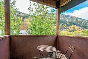 Ein Balkon mit Tisch und Stuhl mit Blick auf einen bewaldeten Hügel.