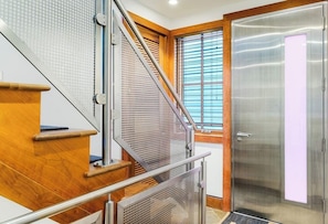 Eine Treppe mit Holzboden und Metallgeländern, eine Glastür eines Aufzugs und ein Fenster mit Jalousien.