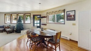 A dining area with a wooden table and chairs, a Christmas tree, and a poster on the wall. - Cozy mountain-view house with full kitchen, dog-friendly & convenient location (Winter Park)