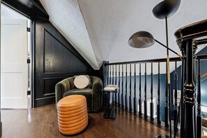 A room with a dark wooden floor, a green armchair, a round ottoman, a small table with a lamp, and a staircase with black balusters. - Spacious home w/ private hot tub, modern kitchen, grill & great location (Edwards)