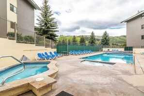 Ein Poolbereich mit zwei Pools, blauen Liegestühlen und Blick auf Bäume und Hügel.