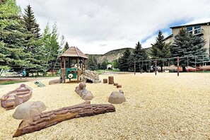 Ein Spielplatz mit einer hölzernen Spielkonstruktion, einer Kletterwand und einem Baumstamm.