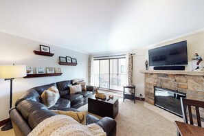 Ein Wohnzimmer mit einer Ledersofa, einem Flachbildfernseher, einem Kamin und einem großen Fenster.