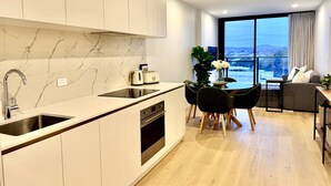 A modern kitchen with a built-in oven, a dining area with a table and chairs, and a large window offering a city view.
