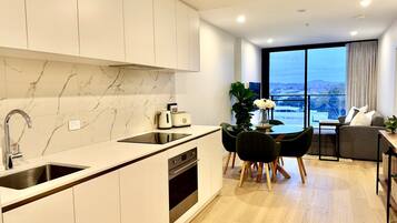 A modern kitchen with a built-in oven, a dining area with a table and chairs, and a large window offering a city view.