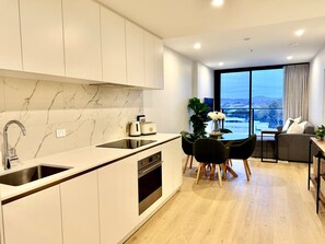 Een moderne keuken met een inbouwoven, een eethoek met tafel en stoelen, en een groot raam met uitzicht op de stad.