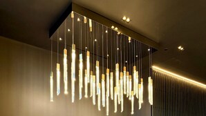 A reception area with a modern design, featuring a dark wall with the name 'THE SHARD' illuminated in gold, two blue chairs, a small round table, and a unique hanging light fixture.