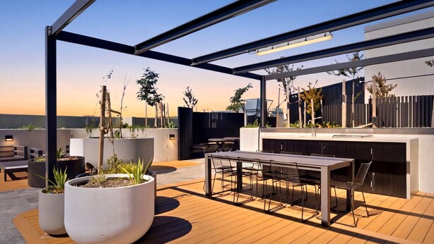 A rooftop patio with a dining table and chairs, potted plants, and a modern outdoor kitchen.