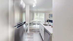 Una cocina moderna con electrodomésticos de acero inoxidable, un comedor con mesa y sillas blancas, y un amplio ventanal que proporciona luz natural.
