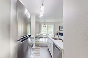 Eine moderne Küche mit Edelstahlgeräten, einem Essbereich mit weißem Tisch und Stühlen sowie einem großen Fenster, das für natürliches Licht sorgt.