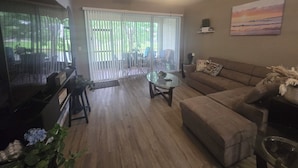 A living room with a sofa, a glass coffee table, a television, and a sliding glass door leading to an outdoor area. - Bright & Airy 3-bdrm near attractions w/ gorgeous community pool in Kissimmee (Kissimmee)