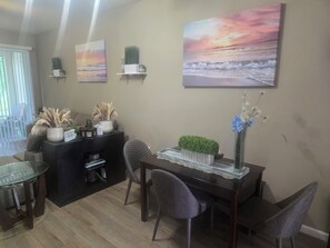 Een eethoek met een tafel, stoelen, een decoratieve plant en wanddecoratie.