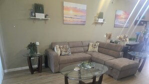 A living room with a sectional sofa, a glass coffee table, and decorative items on shelves. - Bright & Airy 3-bdrm near attractions w/ gorgeous community pool in Kissimmee (Kissimmee)