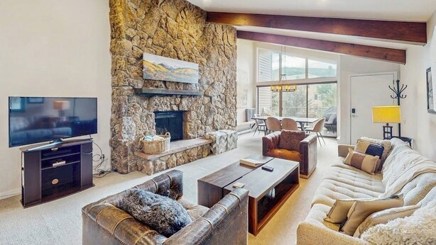 Una sala de estar con pared de piedra, chimenea, televisor y zona de estar.