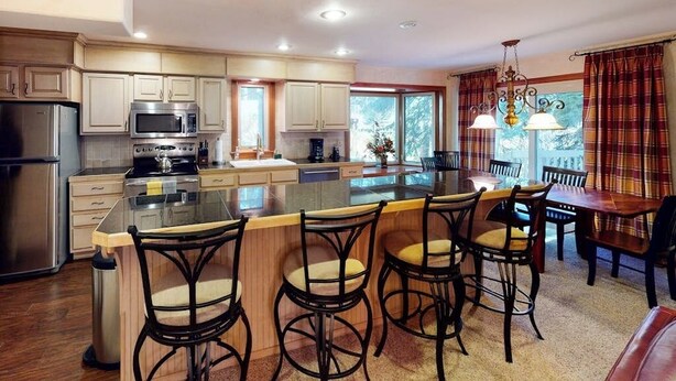 A modern kitchen with a central island, bar stools, and a dining area with a table and chairs. - Creekside Condo w/ Deck: Short Drive to Skiing, Vail Village & Golf (Vail)