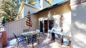 An outdoor patio with a grill, a table with chairs, and a striped umbrella. - Creekside Condo w/ Deck: Short Drive to Skiing, Vail Village & Golf (Vail)