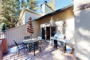 Eine Terrasse im Freien mit Grill, Tisch und Stühlen sowie einem gestreiften Sonnenschirm.