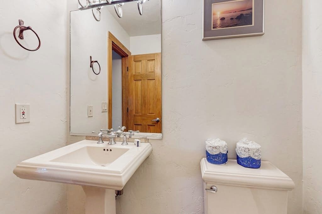 Casa de banho com lavatório, espelho, sanita e um quadro emoldurado na parede.
