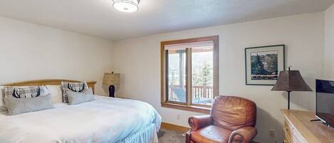 A bedroom with a bed, a leather chair, a dresser, a lamp, a TV, and a window with a view.