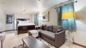 A modern living room with a sofa, a coffee table, a lamp, a bed, and a wall-mounted TV.