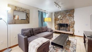A living room with a sofa, a coffee table, a fireplace, a lamp, and a television.