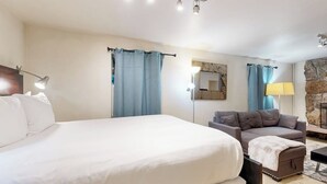 A hotel room with a large bed, a sofa, a lamp, and a stone accent wall.