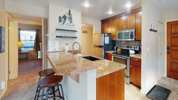 Una cocina con encimeras de granito, armarios de madera, refrigerador de acero inoxidable, microondas y horno.