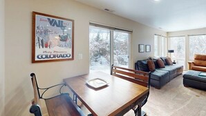 Un comedor con una mesa y sillas de madera, un sofá y un ventanal con vistas a árboles nevados.