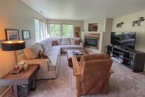 Ein Wohnzimmer mit Ecksofa, Kamin, Fernseher und Bücherregal.