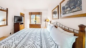 Une chambre à coucher avec un lit, une télévision, une fenêtre et des tableaux encadrés accrochés au mur.