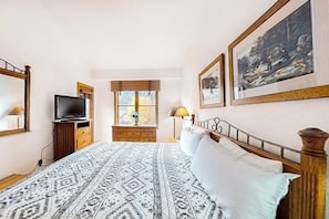 Ein Schlafzimmer mit einem Bett, einem Fernseher, einem Fenster und gerahmten Bildern an der Wand.