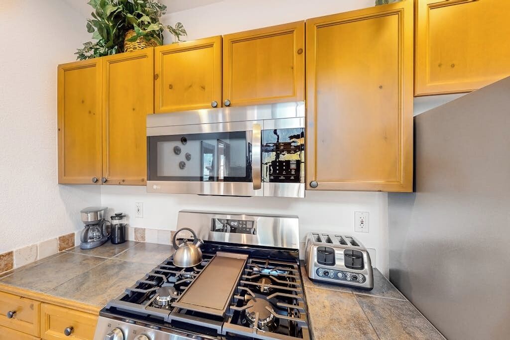 A kitchen with wooden cabinets, a stainless steel microwave, a gas stove, and a toaster.
