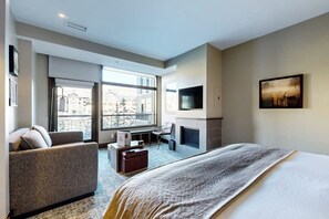 Ein modernes Hotelzimmer mit einem großen Bett, einer Sitzecke, einem Schreibtisch, einem Kamin und einem Fernseher.