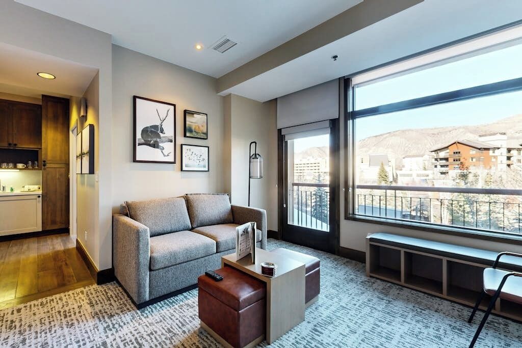 A modern living room with a sofa, coffee table, and a view of a mountainous landscape through large windows.