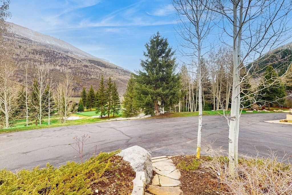 A parking lot with a stone pathway leading to a building, surrounded by trees and a mountain in the background.