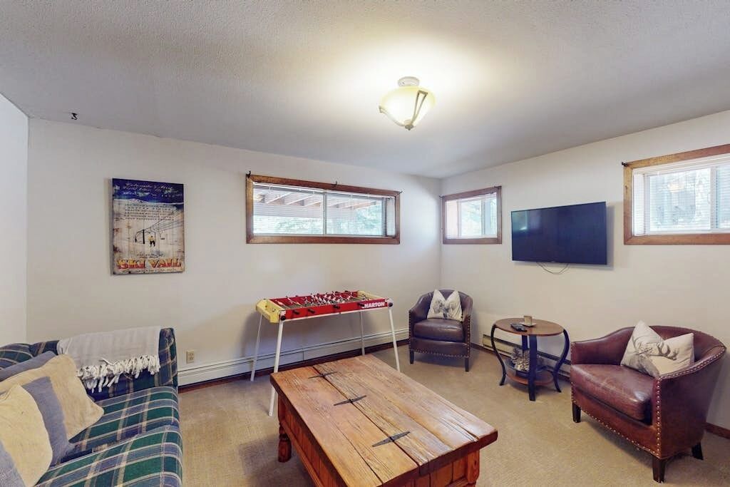 A living room with a sofa, a coffee table, a foosball table, a TV, and a chair.