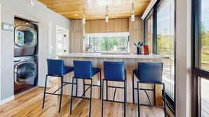 Une cuisine moderne avec un plafond en bois, des tabourets de bar et une grande fenêtre.