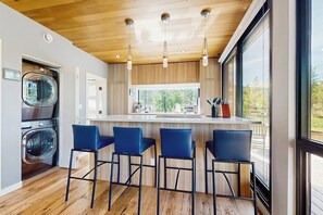 Eine moderne Küche mit Holzbalkendecke, Barhocker und einem großen Fenster.