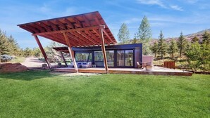 Une structure extérieure moderne dotée d’une paroi vitrée, d’une terrasse en bois et d’un toit en métal.