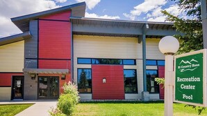 Ein modernes Gebäude mit roter und beiger Fassade, einem Schild mit der Aufschrift 'Hi Country Haus Recreation Center Pool' und einem gepflegten Rasen.