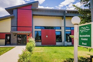A modern building with a red and beige facade, a sign for 'Hi Country Haus Recreation Center Pool,' and a well-maintained lawn. - Mtn-view condo with in/out pools, hot tub, fireplace, great views, rec center (Winter Park)