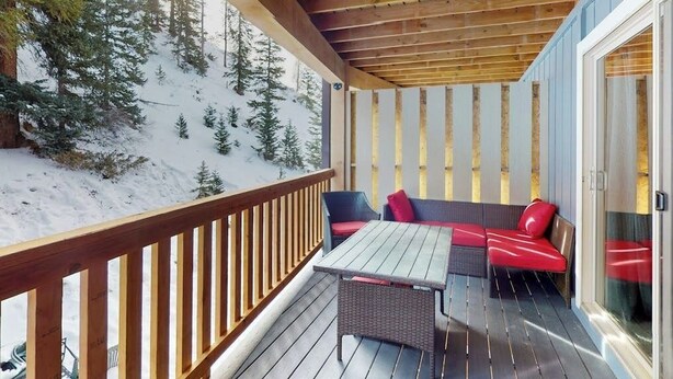 Eine Holzdachterrasse mit Tisch und Sitzgelegenheiten, mit Blick auf eine verschneite Landschaft mit Bäumen.
