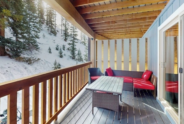 A wooden deck with a table and seating, overlooking a snowy landscape with trees. - Mtn-view condo with in/out pools, hot tub, fireplace, great views, rec center (Winter Park)