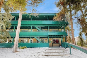 A multi-story building with a green exterior, a staircase leading to the entrance, and a sign indicating the number 10. - Conveniently located condo w/ shared pool, hot tub, game room, fitness area (Winter Park)