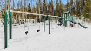 Um parquinho coberto de neve, com balanços e um escorrega.